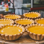 Freshly baked Hong Kong-style egg tarts with a golden, flaky crust and smooth, glossy custard filling, served on a plate. A classic Cantonese dessert popular in dim sum restaurants and bakeries